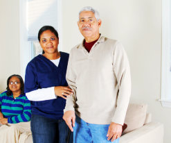 caregiver and senior man standing while senior woman sitting on the sofa smiling