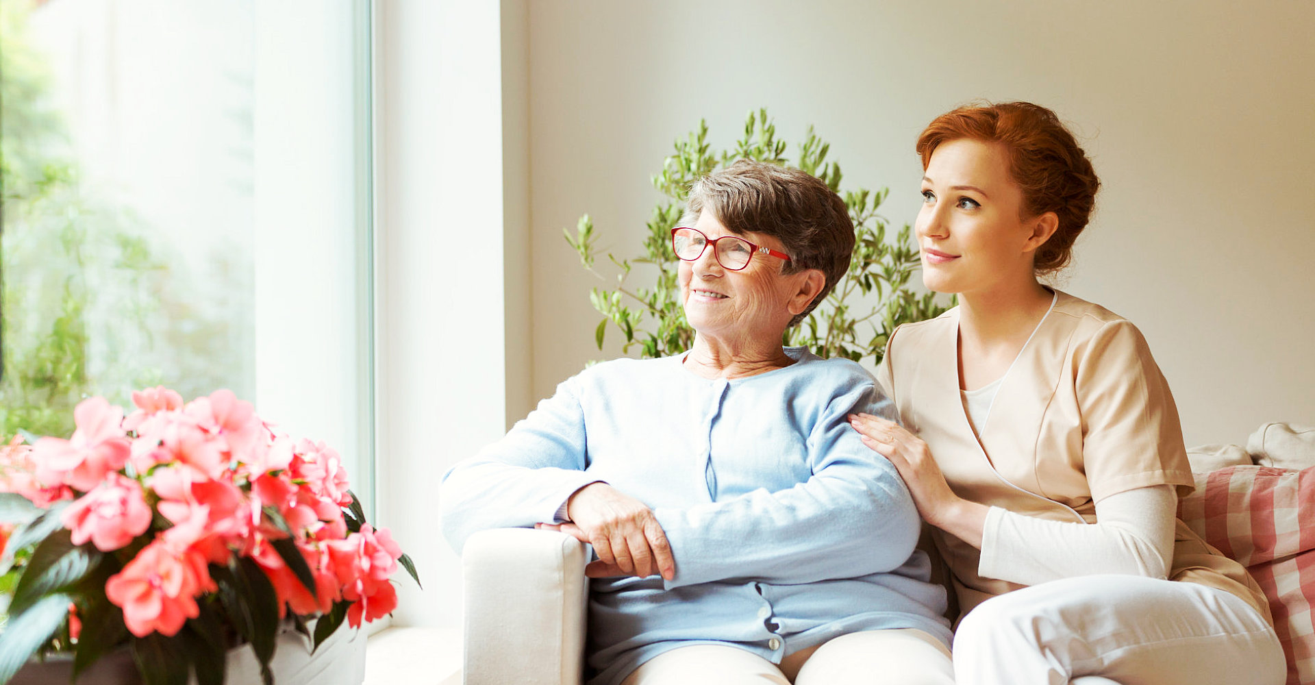 caregiver and senior woman wearing eyeglasses sitting on the sofa smiling